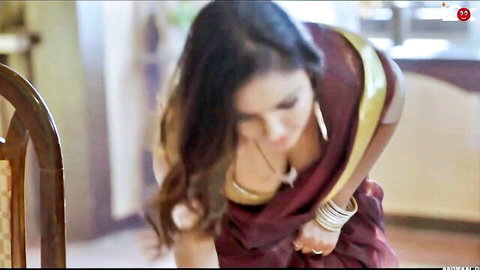 Desi woman in red saree bending forward, revealing deep cleavage