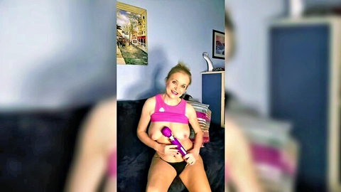 Blonde with big bare tits holding purple vibrator squeezed in cleavage wearing pink panties