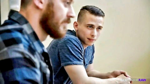 Muscular bearded gay hunk in plaid shirt stares intensely at fit young stud in blue tee