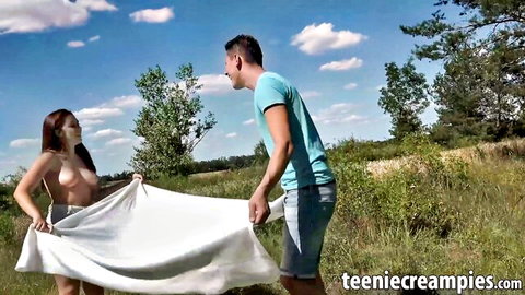 Topless brunette teen holds white sheet over pussy with clothed guy outdoors