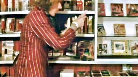 Vintage curly-haired figure in red pinstripe suit browsing adult videos