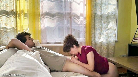 Curly-haired MILF leaning over young man for oral sex on bed