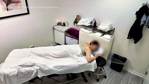Petite East Asian brunette in white bra lies sideways on massage table covered by sheet in erotic massage room