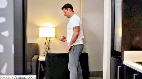 Tattooed hunk in white tee and grey sweatpants holds phone in modern kitchen
