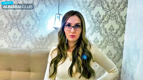Sexy brunette with glasses and long hair in tight sweater posing on couch
