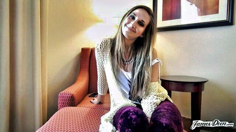 Sexy blonde in open white cardigan and purple pants smiling on red hotel chair