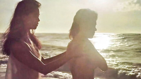Silhouetted Filipino women embracing topless on sunset beach