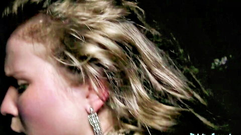 Close-up side profile of blonde with messy wet hair and intense expression wearing dangling earrings