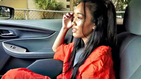 Aria Skye in car, seductive side glance in orange top, long dark hair