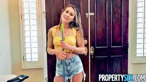Brunette babe in tiny frayed denim shorts and braless yellow tank top holding green feather duster by bedroom door