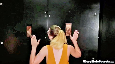 Blonde babe with glasses reaches hands toward two cocks in glory holes