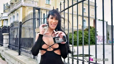 Curvy brunette in revealing black cutout dress smoking outside gate