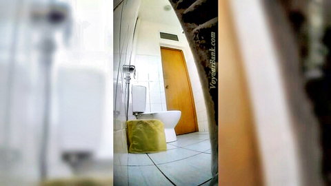 Voyeur hidden cam captures empty public bathroom toilet with yellow cushion on white porcelain seat.