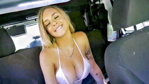 Blonde babe with huge tits spilling from white sling bikini smiling in car backseat