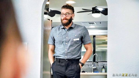Bearded man in gray uniform shirt and black pants stands in locker room bathroom