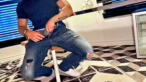 Muscular guy in ripped jeans pulls down waistband teasing his bulge on stool