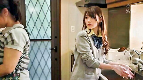 Two Japanese schoolgirls in uniforms washing hands and dishes in kitchen