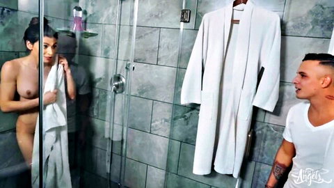 Tanned trans brunette with big dick nude in shower holding towel over medium tits as muscular man watches