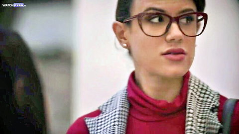 Sexy brunette teacher in red glasses and turtleneck stares seductively at camera