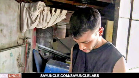 Young Latino twink in black tank top gazing down in workshop, Sploogers Club gay scene