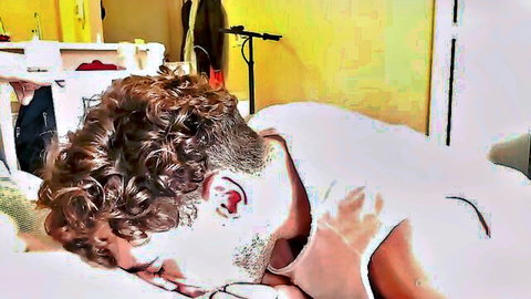 Curly haired twink lies face down asleep with open white shirt exposing chest in yellow bedroom