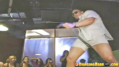Male stripper in tight white shorts dances on stage as excited women cheer at CFNM party