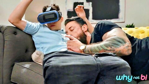 Tattooed bearded guy intimately kisses neck of VR headset-wearing young man in bisexual prelude