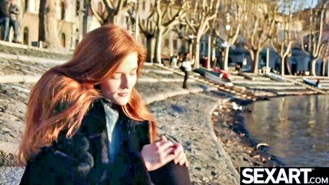 Stunning young redhead with long hair smiling seductively by lake in fur coat