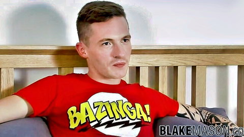 Tattooed young gay guy in red Bazinga t-shirt poses solo on bed for Blake Mason