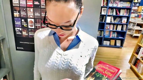 Sexy Asian woman in glasses and sweater holding Kama Sutra book in library showing cleavage