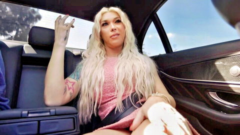 Tattooed blonde trans woman spreads legs wide in car backseat exposing big erect cock