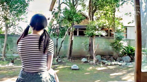Petite pigtail girl in striped top and short pink skirt standing in lush garden outdoors