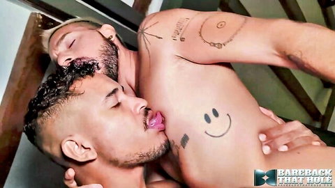 Two hairy tattooed Latino hunks passionately kissing and licking necks in intense bareback embrace