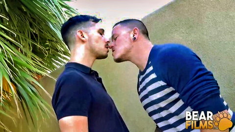 Two muscular Latino men passionately kissing in casual shirts