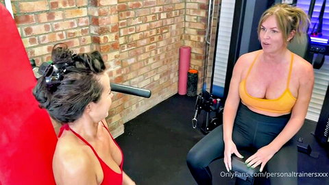 Busty brunette and blonde MILFs in tight gym tops flaunt deep cleavage chatting in fitness gym