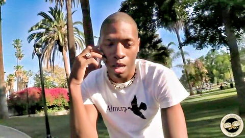Black man in Amir bird t-shirt talking on phone in sunny palm tree park