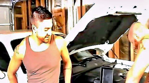 Two muscular young gay men in tight tank tops working on car hood in garage