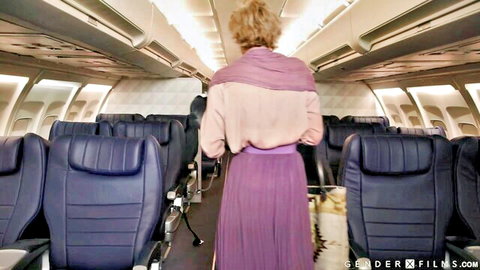 Ariel Demure as blonde trans stewardess in purple skirt walking airplane aisle