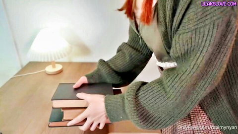 Redhead babe in open green cardigan teasing cleavage while holding books on desk POV