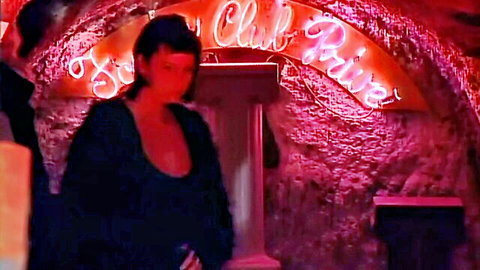 Seductive brunette in low-cut black dress at neon-lit club entrance