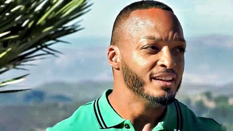 Handsome black man with goatee smiling in green polo shirt outdoors with palm trees and mountains