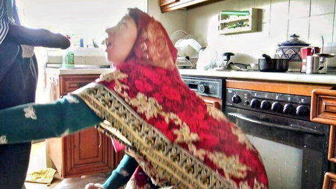 Persian hijab woman in kitchen opens mouth wide as man feeds her hand