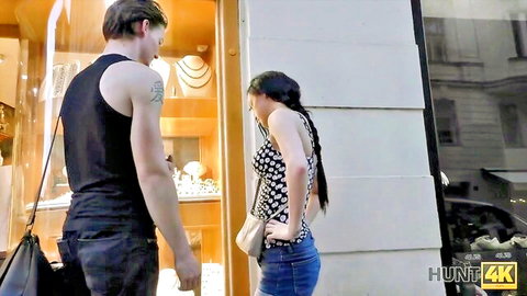Brunette in tight jeans and crop top bends over looking at jewelry store window with muscular guy behind her