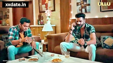 Two fit Indian men chatting on couch in casual shirts, one on phone