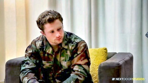 Young freckled brunette soldier in camo uniform sits pensively on couch