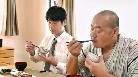Young Japanese man in white shirt eating rice with bald older Asian man in yukata at dinner table