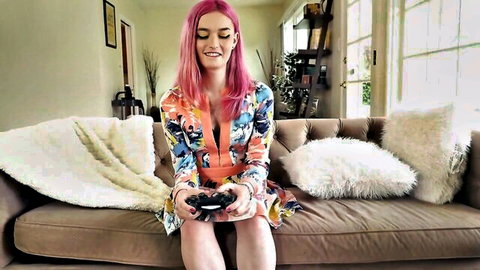 Trans starlet Natalie Stone in low-cut colorful dress, pink hair, holding game controller