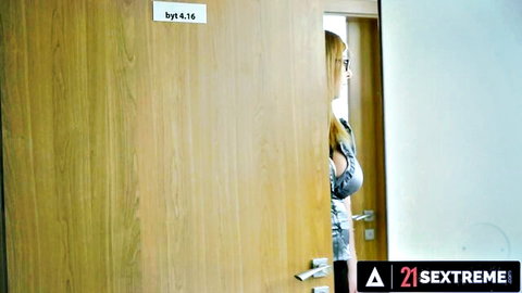 Mature blonde with glasses peeking seductively from behind bedroom door teasing viewers