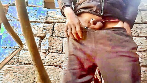 Skinny South Asian guy exposes hard cock and balls from open pants outdoors on stone wall