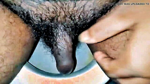 Thick ebony cock with bushy pubes gripped by hand over blue bowl in handjob